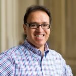 Khaled Mattawa smiles wearing dark glasses and a plaid shirt.