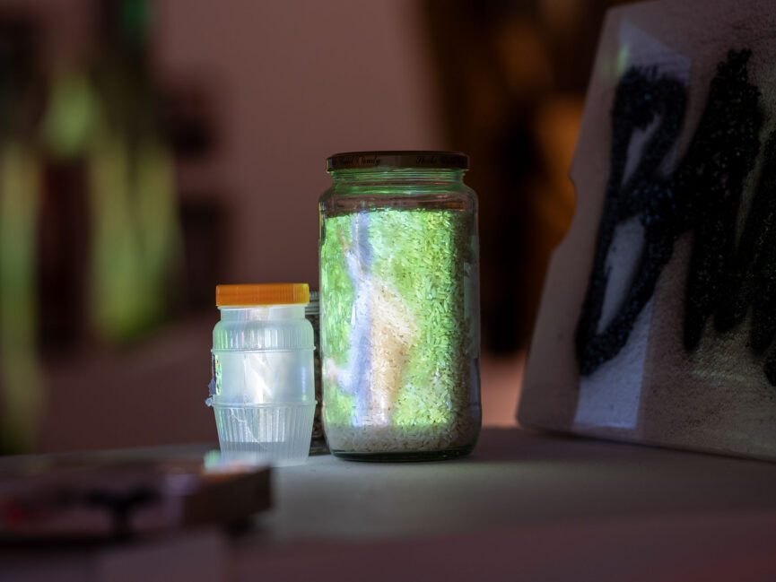 A jar is lit up by a projection on a pedestal in a gallery