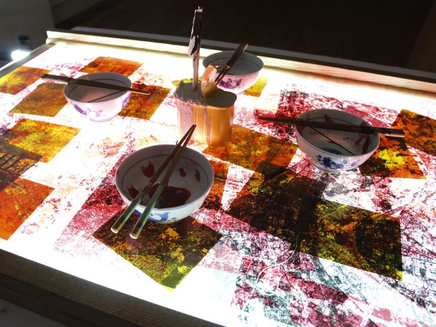 Four place settings featuring bowls and chopsticks sit on a lighted table covered in splatter paint.