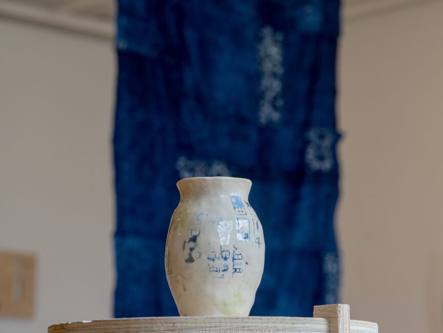 A piece of pottery sit in front of a hanging drapery in a gallery