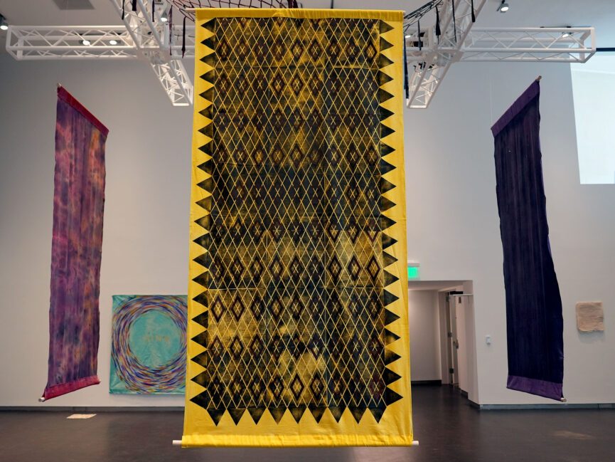 Large tapestries hang from the ceiling and the walls in a large gallery space