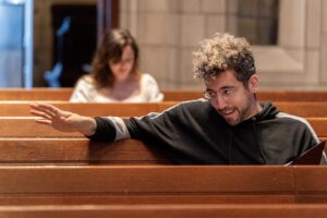 Heath Saunders reads from a script and gestures while seated in the Princeton University chapel pews.