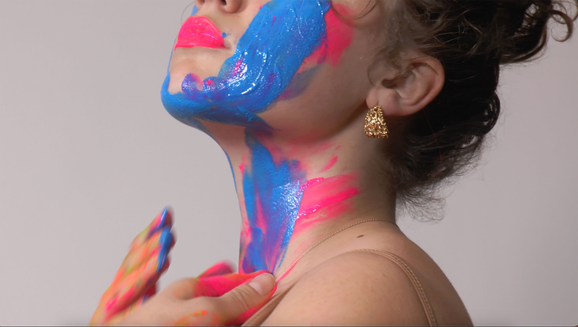 A person seen in profile applies pink and blue paint to their neck and face.