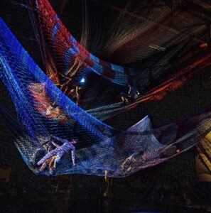 Dancers move in colorful nets suspended above the ground.
