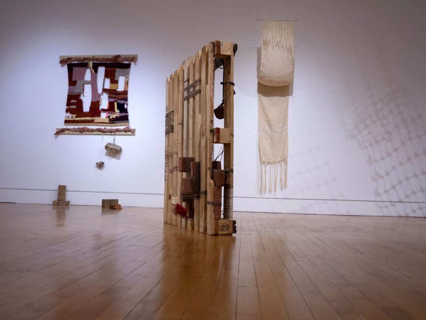 Artwork sits on the floor and hangs on the walls of a gallery