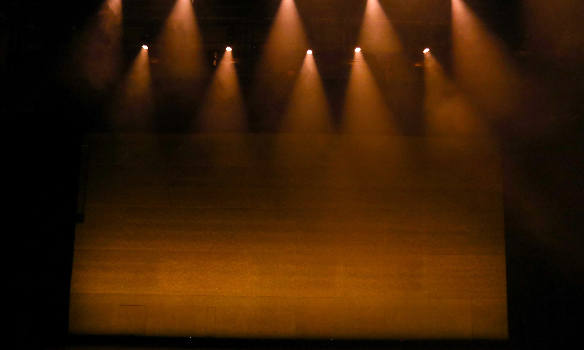 A dark theater stage illuminated by several warm, amber spotlights.