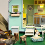 World of miniature including a tiny house with bed, table, chairs, kitchen cabinets, wood/fire and a dog.