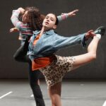 Two dancers balance on one leg with their arms and other leg up in the air.