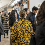 A group of people mingling at an art exhibition with artworks on the walls.