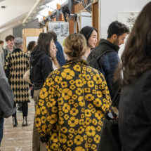 A group of people mingling at an art exhibition with artworks on the walls.