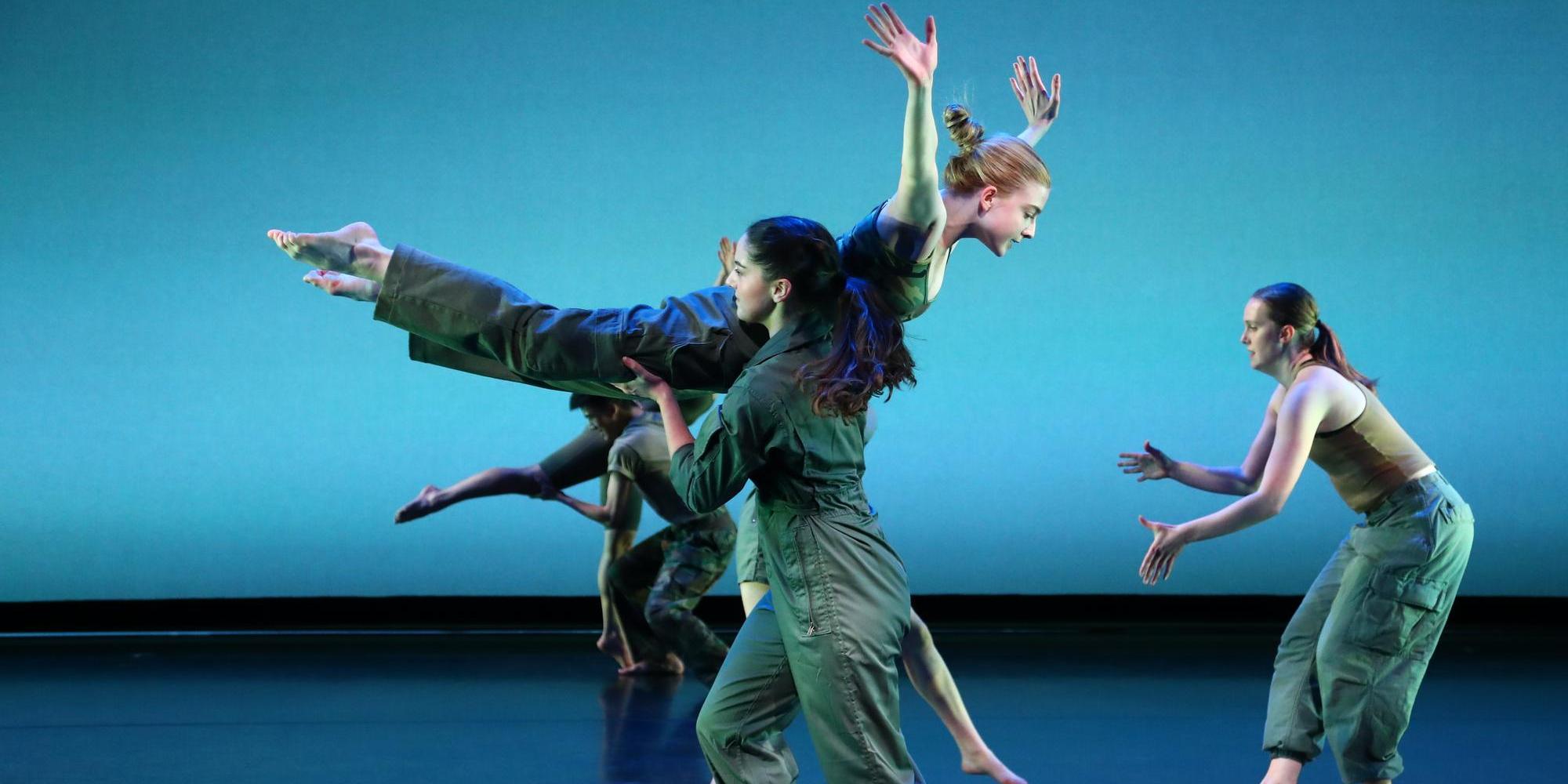 One dancer holds another dancer up in the air, while the airborne dancer has both arms and legs outstretched.