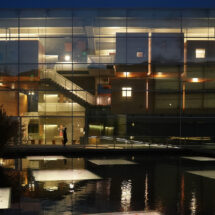 Exterior view of Effron Music building at night, with reflections of light in the water feature in front of the building.