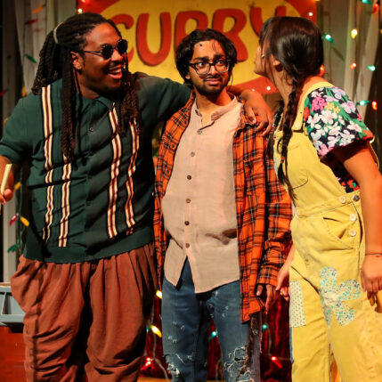 Three people standing on stage in front of a sign and string lights.