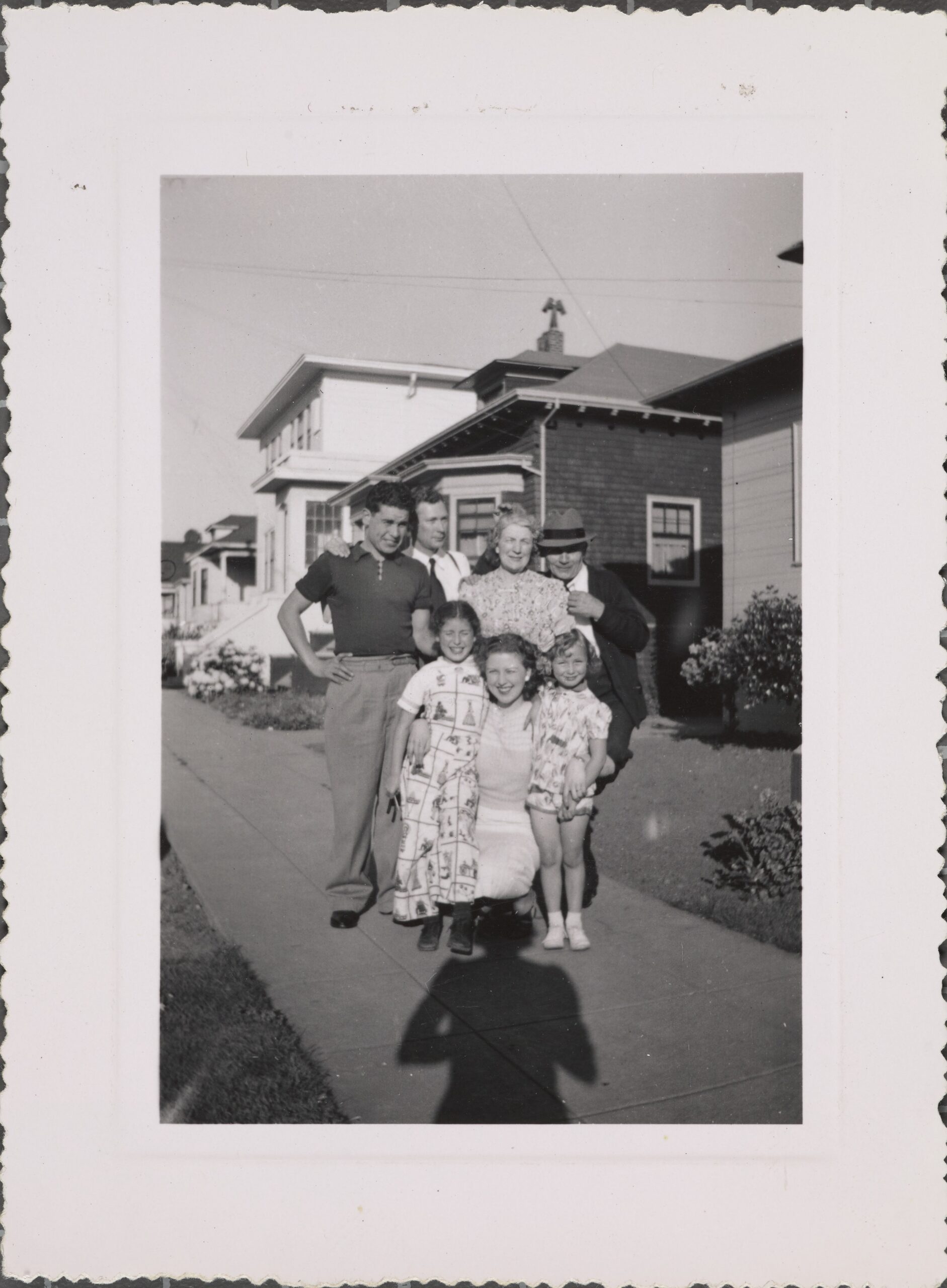 A group of people pose for a portrait. Houses and clothing is from 1940s.