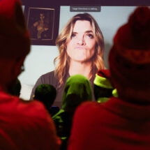 People watching a screen with a woman making a humorous expression. Text reads, “Stage Directions is talking.”