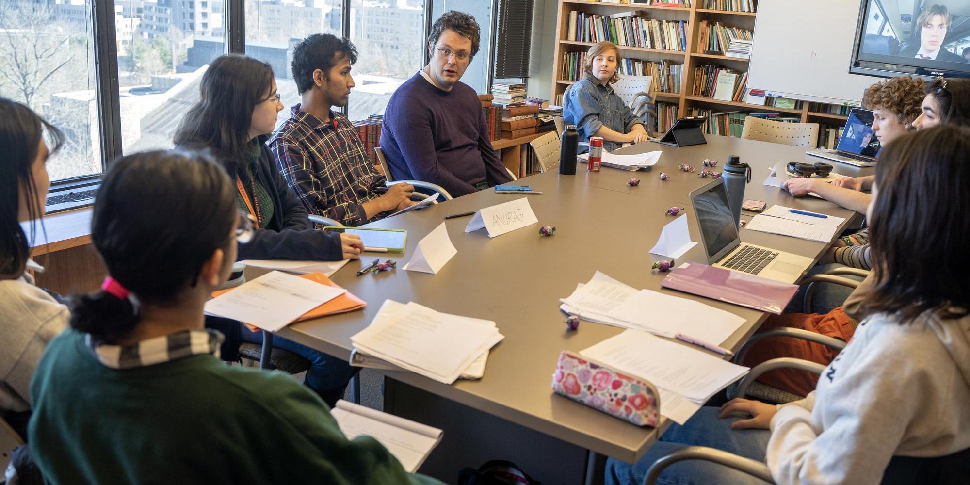 People sit talking around a large table scattered with papers.