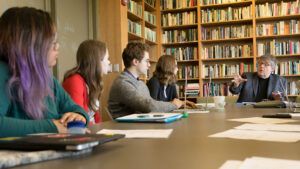 Paul Muldoon sits at a table with students in a library setting.