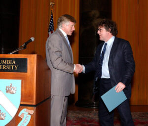 Two people stand near a podium and shake hands.