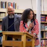 Nicole Sealey speaks into a mic at a podium in a bookstore.